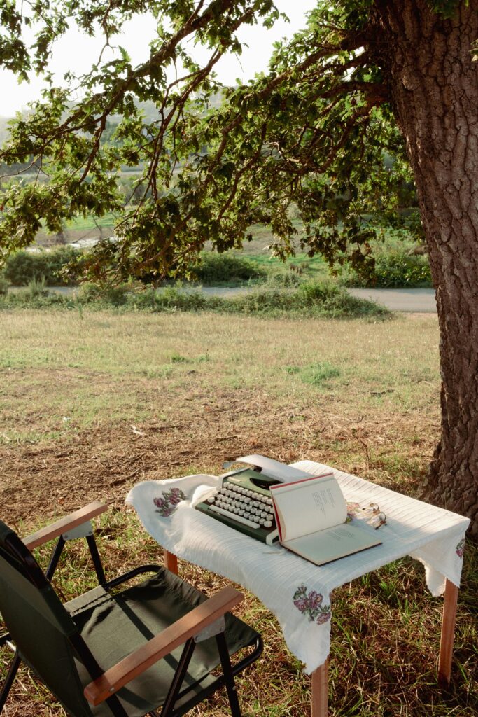 outdoor table and chairs with typewriter and journal under a tree
